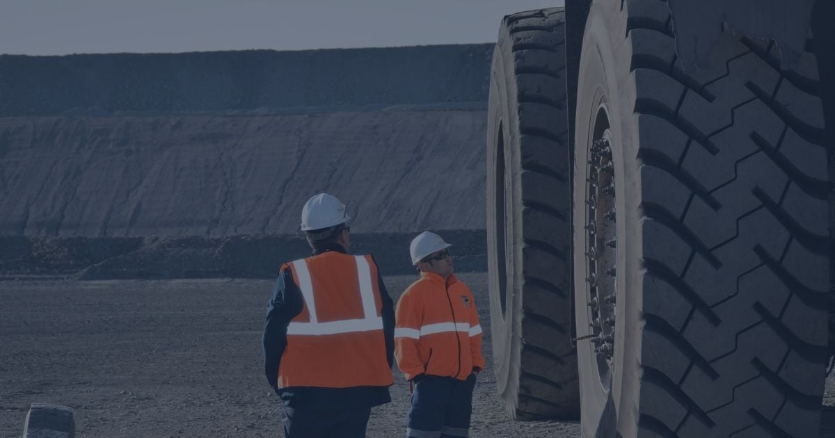 Two mining personnel inspecting the massive tires of a haul truck at an open-pit mine site