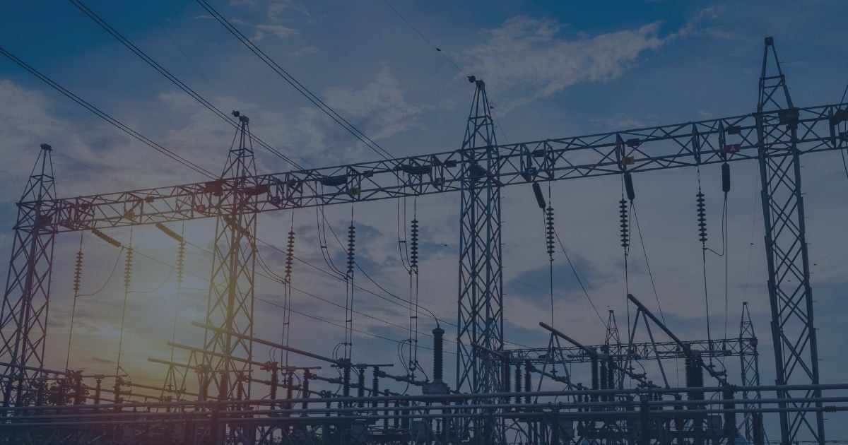 High-voltage electrical substation with transmission towers and power lines silhouetted against a blue sky at sunrise