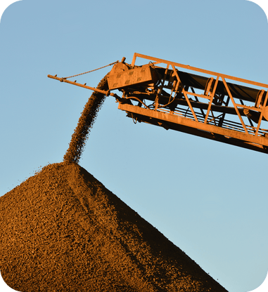 Conveyor belt releasing processed material onto a conical stockpile under clear sky.