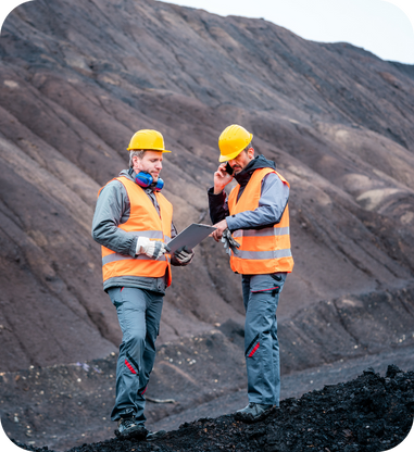Two mining engineers reviewing plans on a tablet in front of a stockpile.