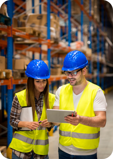 Two engineers reviewing operational data on a tablet in a warehouse, surrounded by shelves and inventory.